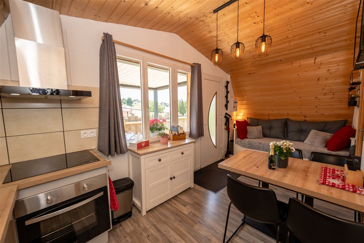Pièce de vie chaleureuse en bois avec cuisine, table et salon du chalet Au Doux Altic